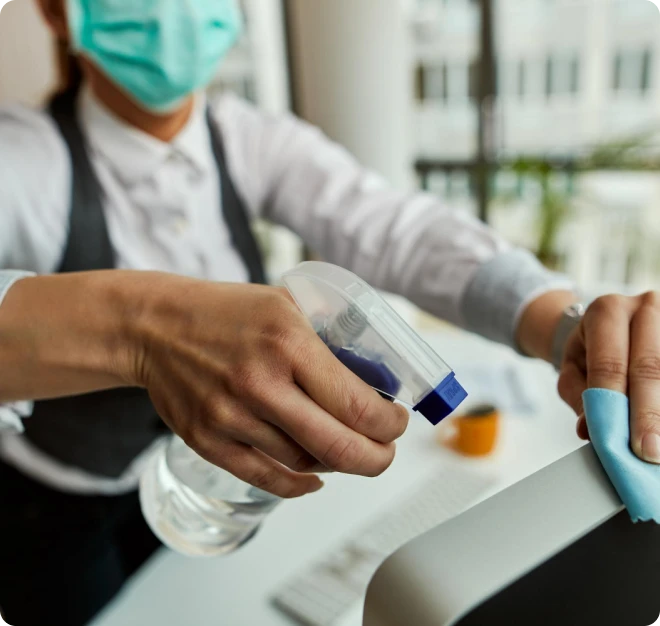 Commercial cleaner wearing a mask and sanitizing office equipment, representing Beeyond Facility Services' expert Commercial Cleaning in Northern Virginia (NOVA Hub).